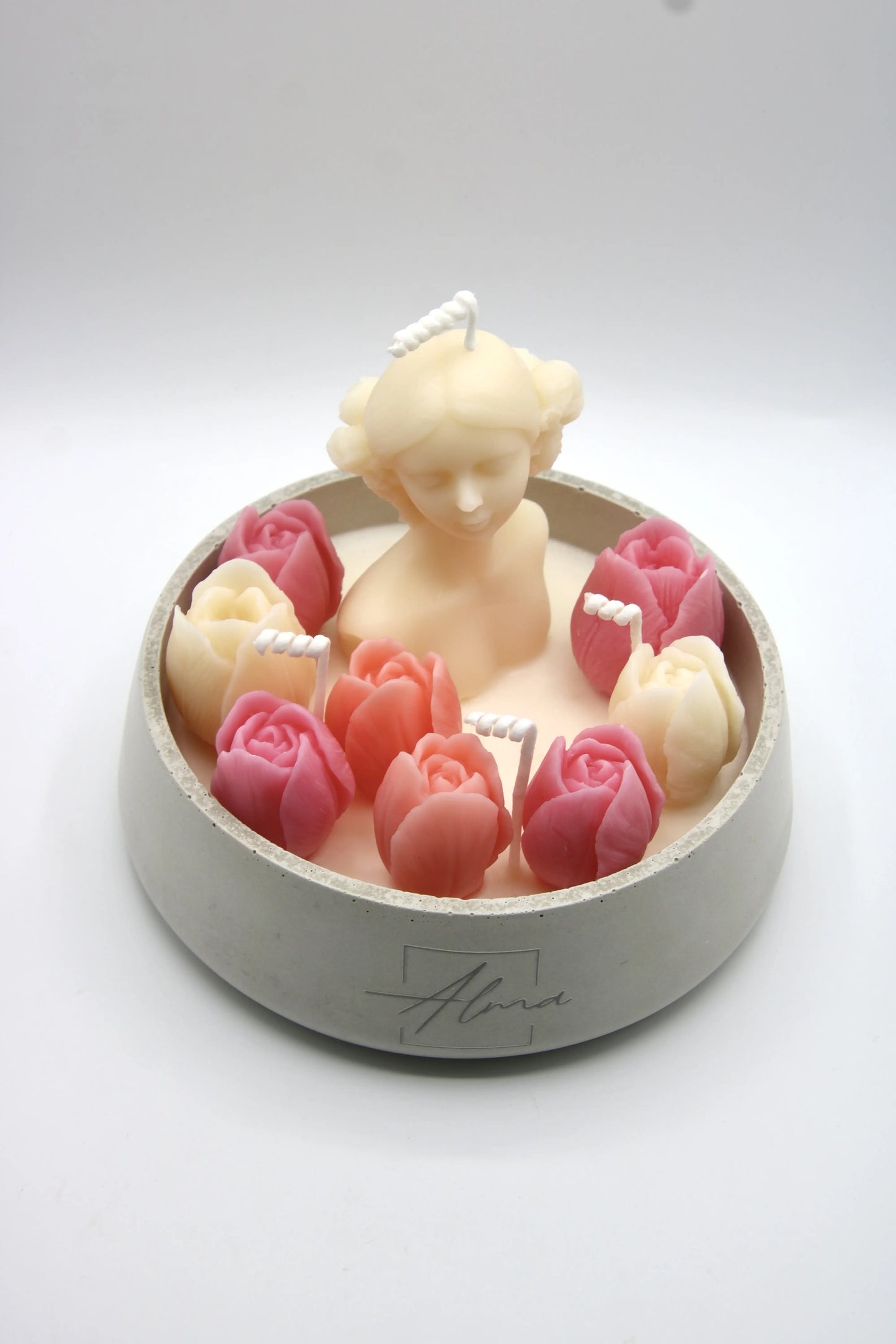 Candle in the shape of a woman surrounded by pink roses on a white background