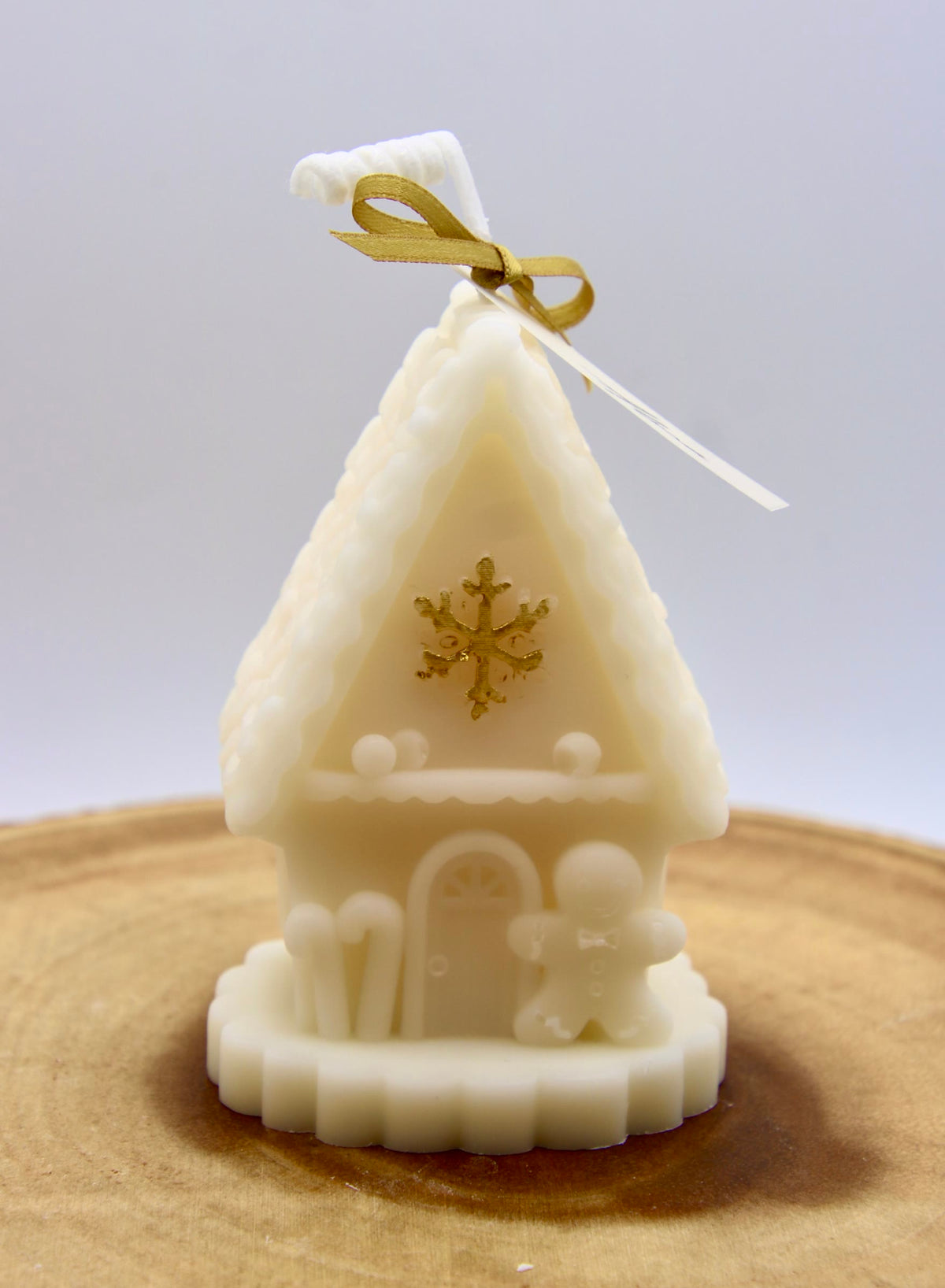 Ivory gingerbread house candle with candy canes, a gingerbread man by the door and a gold snowflake