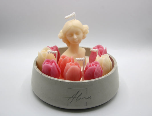 Candle shaped like a woman with pink tulips in a white container on a light gray background
