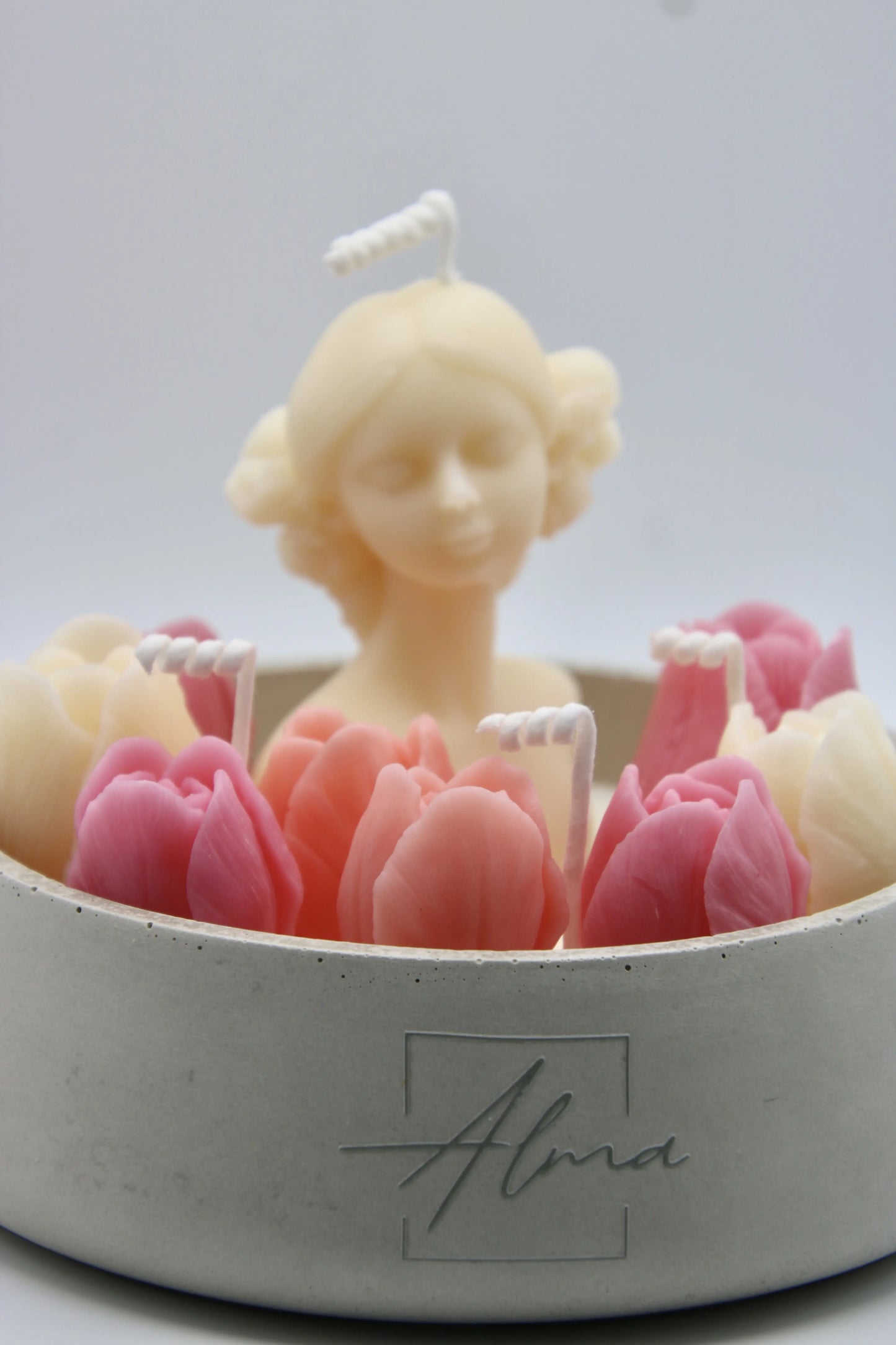 Candle sculpture of a woman with pink tulips in a concrete holder, brand 'Alma' visible.