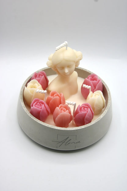 Candle in the shape of a woman surrounded by pink roses on a white background
