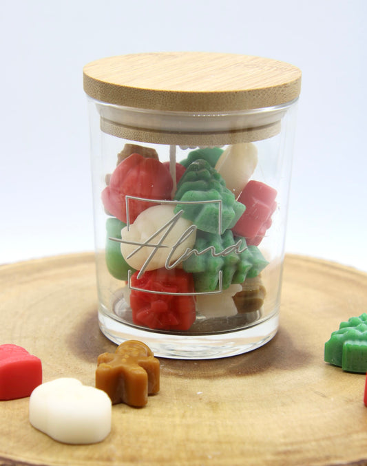Christmas Vibes jar closed with its bamboo lid and the Alma logo on the glass, loose wax shapes around it