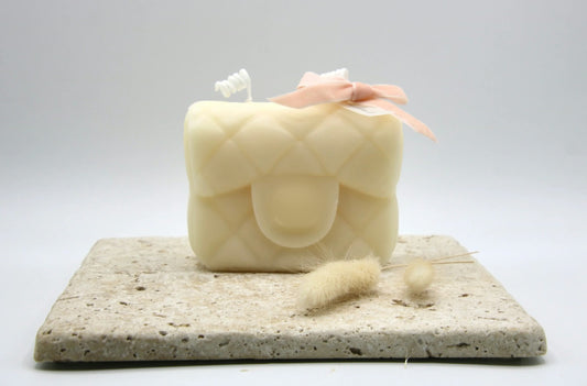 Ivory quilted purse candle with a pink ribbon bow on a stone tile