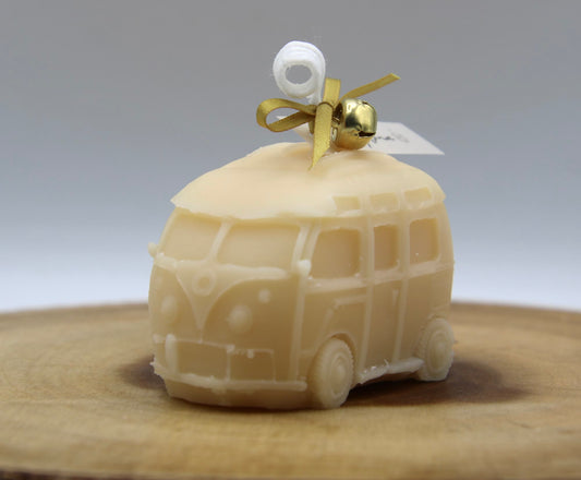 Ivory van candle seen from the front, with a gold ribbon and jingle bell on the roof, on a wood slice