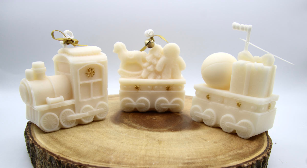 Ivory Christmas train candle in three pieces: an engine and two cars carrying toys and gifts, tied with gold ribbon