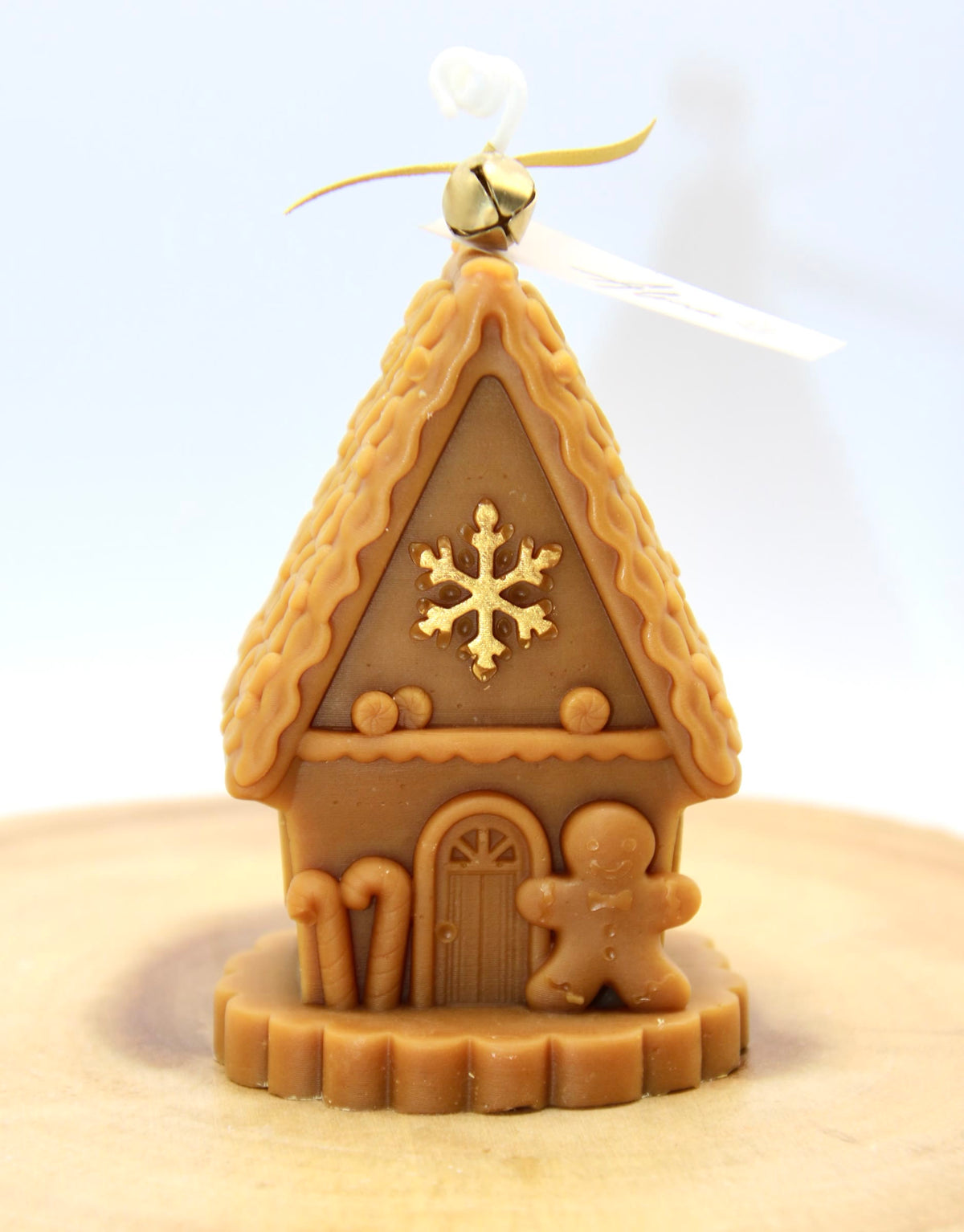 Light brown gingerbread house candle with candy canes, a gingerbread man by the door and a gold snowflake